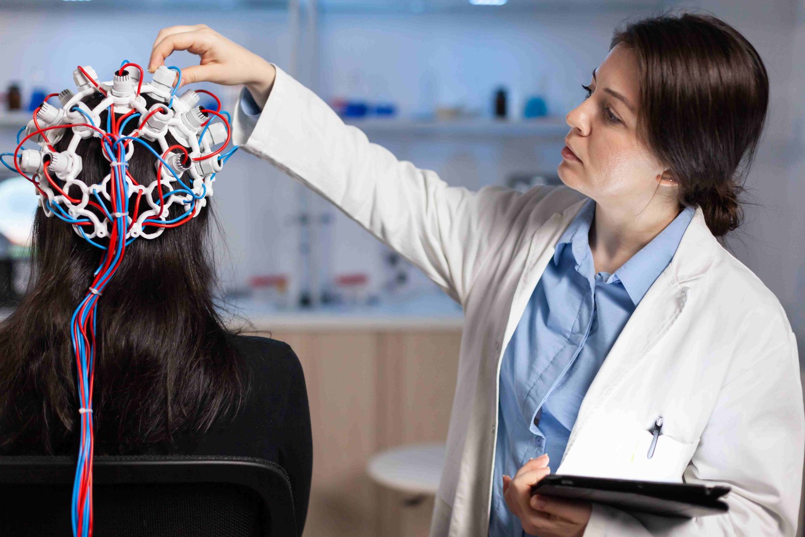 back view woman patient wearing performant eeg headset sitting chair neurological research laboratory while medical researcher adjusting it examining nervous system typing tablet 11zon